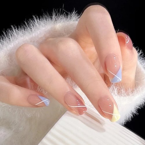 Uñas postizas press-on nude translúcidas crema con bloque de color diagonal amarillo y azul claro, línea blanca fina y brillo sutil. Forma almendra medio-larga, acabado brillante, reutilizables — look minimal diario