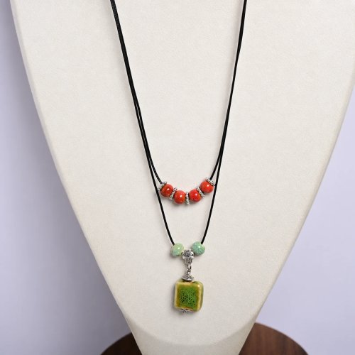 Collier artisanal en perles de céramique avec perles carrées vertes et rouges, cordon ciré et détail métallique